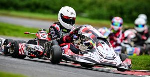 James Kell racing an XKART go kart around whilton mill kart circuit at the kart JKC championship junior rotax red and black and white go kart with driver in white arai helmet